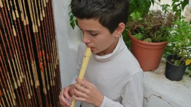 Genç bir çocuk saksı bitkileri ve doğal elementlerle çevrili huzurlu bir bahçe ortamında flüt çalıyor. Odaklanması ve ifadesi, müzik ve sükunete derin bir bağlantı sağlıyor..