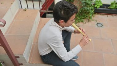 Açıkta oturan genç bir çocuk bir kaydedici çalar. Gündelik ortam ve sakin ifade, müzik keşfi ve yaratıcılığın bir anını yakalıyor..