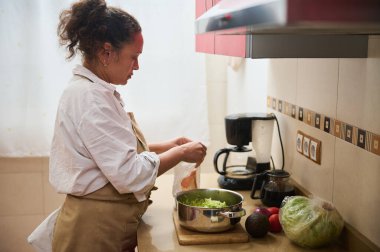 Sıcak mutfak ortamında, taze sebzeli sağlıklı yeşil bir salata hazırlayan bir kadın. Sahne sakin ve evcimen, ev yemeklerini ve sağlıklı beslenmeyi ön plana çıkarıyor..