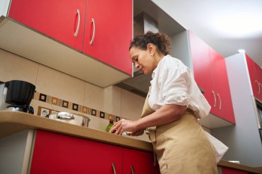 Çağdaş bir mutfakta yemek pişiren, kırmızı dolaplar ve modern aletlerle yemek hazırlamaya odaklanan bir kadın. Günlük ev yemeği atmosferi.