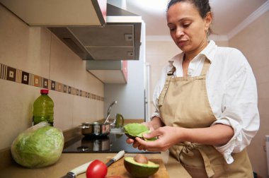 Mutfakta bir kadın taze malzemelerle çevrili bir avokadoyu dikkatlice soyuyor. Önlük takıyor, sağlıklı yemek ve yemek hazırlama üzerine yoğunlaşıyor..