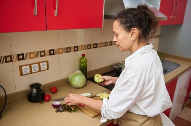 Çağdaş bir mutfakta sebze doğrayan bir kadın. Renkli dolaplar ve taze ürünler, sağlık ve ev hayatını ön plana çıkaran canlı bir yemek atmosferi yaratıyor..