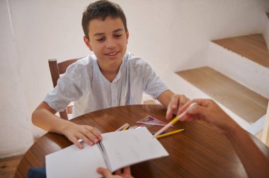 Genç bir çocuk ahşap bir masada eğitici bir iş üzerinde çalışırken gülümser, kırtasiyeyle yaratıcı bir şekilde ilgilenir..