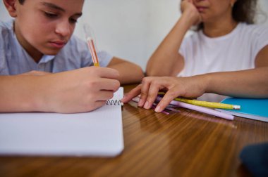Genç bir çocuk, akıl hocası izlerken bir deftere yoğun bir şekilde yazar. Kurulum odaklanmayı ve teke tek öğrenmenin önemini, eğitim danışmanlığını vurguluyor.