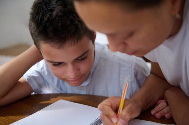 Şefkatli bir anne, oğluna mutfak masasında ödevlerinde yardım eder. Konsantrasyon ve destek sağlar..