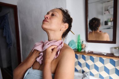 Havluya sarılmış bir kadın kendini banyoda pembe bir havluyla kurutuyor. Rahatlama ve kendine dikkat etme hissi yayıyor..