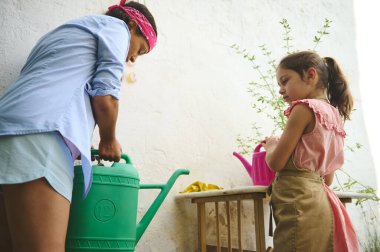 Bir anne ve kız bahçıvanlığın, yeşil ve pembe sulama kutularıyla sulamanın tadını çıkarırlar. Yeşillik bahçesinde sıcak bir bağ etkinliği..