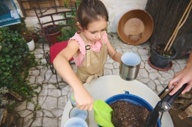 Genç bir kız verandadaki toprak ve konteynırları dikkatle kullanıyor. Heyecanı ve odaklanması, doğaya ve bahçecilik faaliyetlerine olan sevgisini gösteriyor. Sabır ve özeni öğretiyor..
