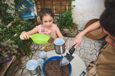 İki çocuk dışarıda bahçıvanlık yapıyor, çömleklere tohum ekiyor. Odaklanıyorlar ve doğal aktivitenin tadını çıkarıyorlar. Yeşillik bahçelerinde önlük giyiyorlar..