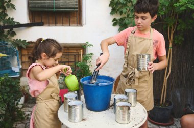 Two children in aprons enjoy a gardening project. They prepare pots with soil in an outdoor setting, promoting teamwork and learning. Vibrant and educational, perfect for family-themed concepts. clipart