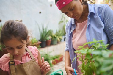 Bir anne ve kız, canlı bir ev bahçesinde, bitkileri besleyen ve bağ kuran bir anı paylaşıyor. Sahne, sabır, özen ve doğayla bağlantıyı yakalar..