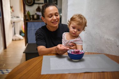 Sevgi dolu bir büyükanne, küçük torununu ahşap yemek masasında besler. Sıcak mutfak dekorasyonu aile sevgisini yansıtan bir yemekten zevk alırken sıcaklığı ve bağlantıyı arttırır..