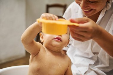 A loving mother shares a joyful bath time with her baby, creating playful and tender moments. The baby uses a yellow scoop, bringing joy and warmth to this intimate scene. clipart