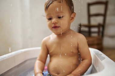 Tatlı bebek keyifli bir banyo yapıyor, su damlacıkları neşeli bir atmosfer yaratıyor. Sıcacık, rahat bir ortamda yakalandılar..