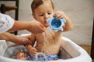 Genç bir çocuk banyo sırasında mavi kaplumbağa şeklinde bir oyuncakla oynuyor. Neşeli sahne, neşeli masumiyeti ve özeni yakalar. Kapalı bir ortamda suyun sıçraması gibi..