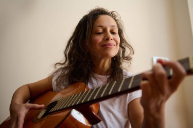 Bir kadın akustik gitar çalmaktan, sakin ve düşünceli bir atmosfer yaratmaktan hoşlanır. Onun ifadesi rahatlamayı ve müzikal tutkuyu yansıtır, yaratıcılığı ve sakinliği parlak bir ortamda somutlaştırır..