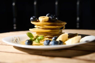 Üzerinde taze yaban mersini ve muz dilimleri olan ev yapımı krep yığını. Pekmezle sulanan bu kahvaltı, tazeliği ve hoşgörüyü simgeliyor..