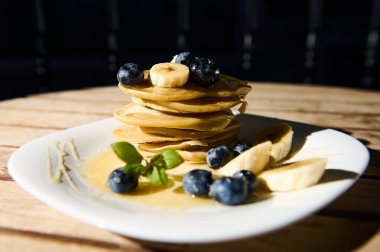Üzerine taze yaban mersini ve muz dilimleri serpilmiş bal serpilmiş ağız sulandıran altın krep yığını. Kahvaltı ya da brunch için mükemmel. Tazelik ve lezzet yayıyor..