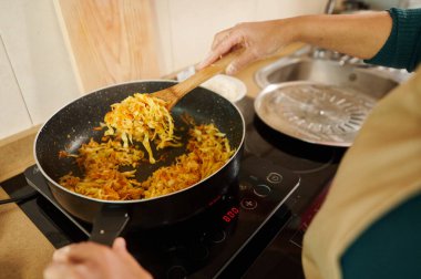 A home cook prepares stir-fried vegetables in a frying pan. The modern kitchen setup enhances the cooking experience, focusing on healthy and flavorful homemade dishes. clipart