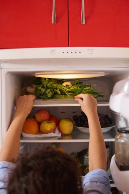 Bir insan canlı, iyi organize edilmiş bir buzdolabında taze meyve ve sebze düzenler. Sahne, gıda deposunda temiz ve düzenli bir yaşam tarzının altını çizerek sağlığa ve ayrıntılara dikkat çekiyor..