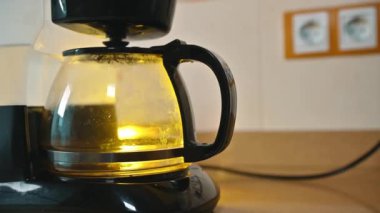 Bir kahve makinesi sıcak sabah ışığıyla aydınlatılmış taze bir kahve demliyor. Görüntü, sıcak bir mutfak atmosferinin özünü yakalıyor. Güne zengin bir aromayla başlamak için ideal..