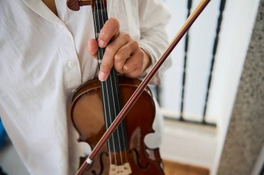 Odanın içinde kemanı tutan bir müzisyenin elleri ve telleri vurguladığı detaylı bir görüntüsü. Çekim, klasik müzik performansının özünü hassasiyetle ve sanatsal açıdan yakalıyor..