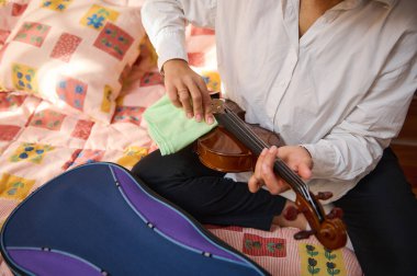 Bir kişi canlı bir yatak örtüsünün üzerinde otururken bir bez ile bir kemanı dikkatlice temizler. Bu görüntü, müzik aletine bir anlık ilgi ve ilgi gösteriyor ve müzik ile kişisel tutku arasındaki bağlantıyı vurguluyor..