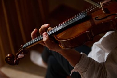 Bir kemancının eli ustalıkla keman çalarken, müzisyen ve enstrümanın zarafetini ön plana çıkaran detaylı bir yakın çekim..