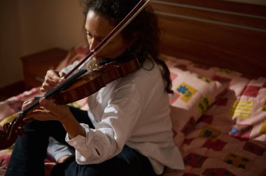 Genç bir kadın yatağında oturmuş keman çalıyor, dikkatle odaklanıyor. Sahne, müzik için sükunet ve tutku yayar. Kapalı bir ortamda yakalanır..