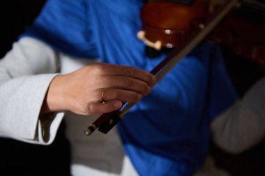 Keman çalan bir elin detaylı bir görüntüsü, canlı bir mavi arka plana karşı müzikal uzmanlığı vurguluyor..