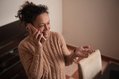 Rahat bir kazak giymiş neşeli bir kadın evde olumlu bir telefon görüşmesi yapıyor. Meşgul ve rahat görünüyor. Bir arkadaşı ya da aile üyesiyle sohbet ediyor..