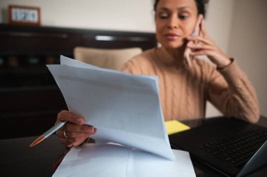 Bir kadın ev ofis masasında aynı anda telefon görüşmeleri ve evrak işleriyle uğraşarak görevlerini başarıyla yerine getiriyor..