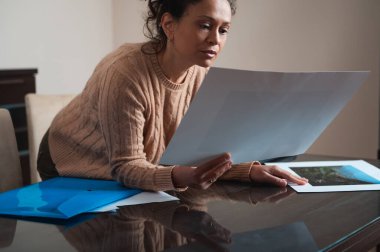 Sıcak kazaklı bir kadın yansıtıcı bir masadaki büyük bir izi yakından inceliyor. Düşünceli tavrı, sakin ve minimalist bir geçmişe karşı odaklanma ve tefekküre dayanıyor..