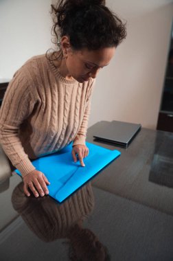 A woman in a cozy sweater carefully wraps a gift in blue paper on a wooden table, focusing on neatness and precision. clipart