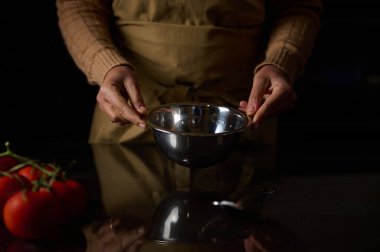 Yanında taze domateslerle karıştırma kasesi olan bir insanın yakın plan çekimi yemek pişirme sahnesi oluşturuyor..