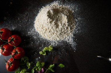 Olgun domatesler ve taze fesleğen yapraklarıyla çevrili bir un yığını. Pizza yapmak ya da pişirmek için ideal..