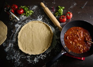 Hamur, domates sosu ve ahşap bir masada taze fesleğenle pizza hazırlama sahnesi..