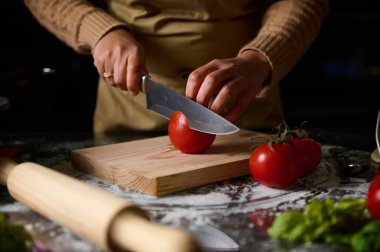 Ev mutfağında ahşap bir tahtada ustalıkla taze domates doğrayan biri. Sahne, yemek pişirme, ev yemeği pişirme ve yemek hazırlamada taze malzeme kullanımını ön plana çıkarıyor..