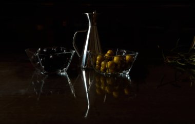 Siyah ve yeşil zeytinleri gümüş bir yağ tenekesinin yanında cam kaselerde sergiliyorlar..