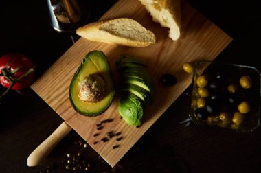 Tahtaya dizilmiş ekmek ve zeytinlerle dilimlenmiş avokado kırsal ve iştah açıcı bir görüntü yaratıyor. Tarifler, yemek blogları veya sağlıkla ilgili içerik için mükemmel.