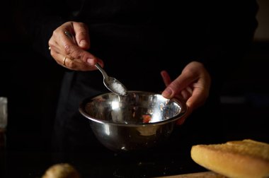 Eller dikkatlice metal bir kaseye malzeme ekleyerek lezzetli bir mutfak sahnesi yaratıyor..