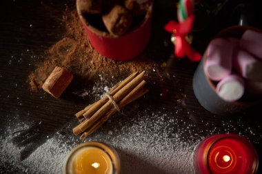 Tarçın çubukları, kakao, marşmelov ve mumların yer aldığı samimi tatil malzemelerinin yukarıdan görünüşü şenlikli ve sıcak bir atmosfer yaratıyor..