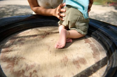 Bir bakıcı olarak yakalanan hassas bir an bir bebeği çocuk parkında lastik salıncakta tutuyor, güvenliği ve keşfi simgeliyor..