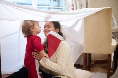 Bir anne ve çocuğunun ev yapımı battaniye kalesinde neşeli bir anı paylaştığı neşeli bir an..