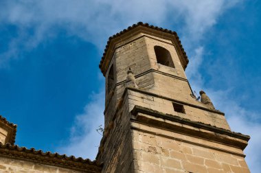 Mimari zerafet ve mirası gözler önüne seren, dağınık bulutlu, parlak mavi gökyüzüne karşı kurulmuş tarihi bir taş kulenin detaylı bir görüntüsü..