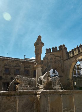 Heykellerle süslenmiş tarihi bir taş çeşme, mavi gökyüzüne karşı kurulmuş. Çeşme karmaşık ayrıntıları içeriyor ve antik mimarinin cazibesini yansıtıyor..