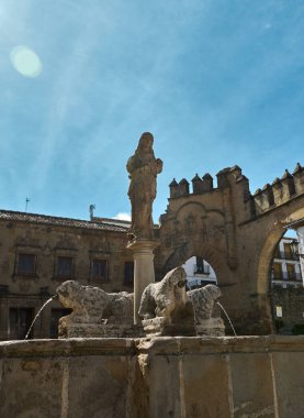 Heykellerle süslenmiş tarihi bir taş çeşme, mavi gökyüzüne karşı kurulmuş. Çeşme karmaşık ayrıntıları içeriyor ve antik mimarinin cazibesini yansıtıyor..