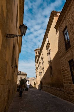 Canlı mavi gökyüzünün altındaki eski taş binalarla çevrili tarihi cadde. Ortaçağ mimarisinin sakin bir ortamda tarih ve kültürü yansıtan resmedilmiş görüntüsü.