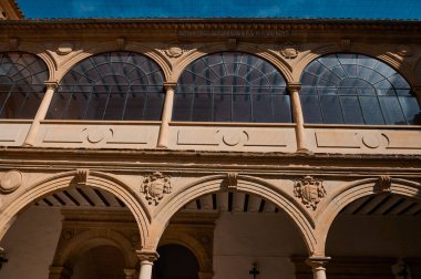 Zarif kemerli pencerelerin ve açık mavi gökyüzü altında karmaşık mimari detayların yer aldığı tarihi bir binanın ön yüzü..