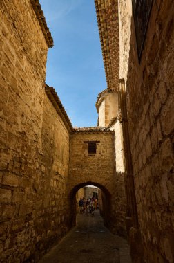 Antik taş duvarları ve parlak mavi gökyüzünün altında insanlarla dolu kavisli bir geçidi olan büyüleyici dar bir sokak..